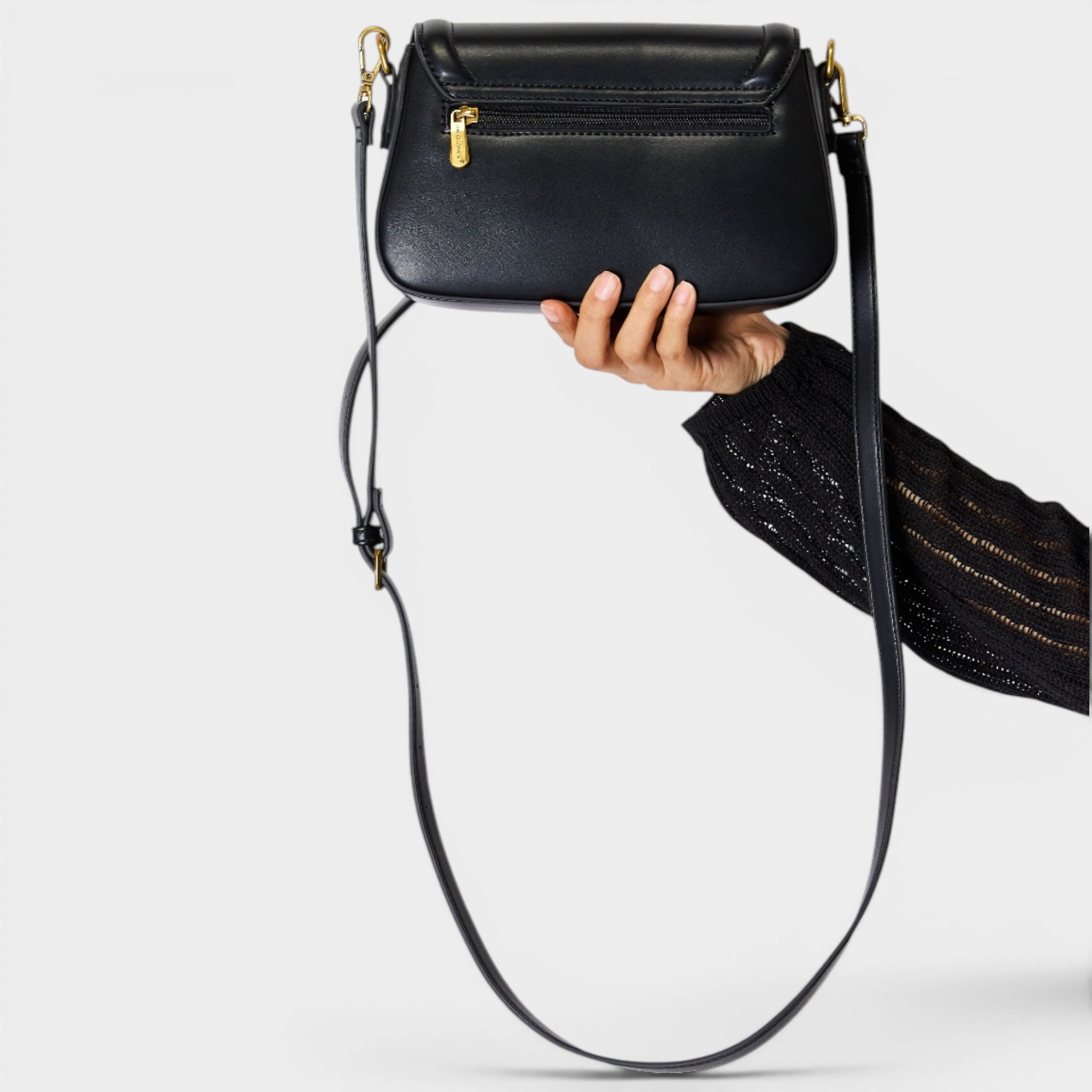 Black handbag with a long strap held by a person on a white background