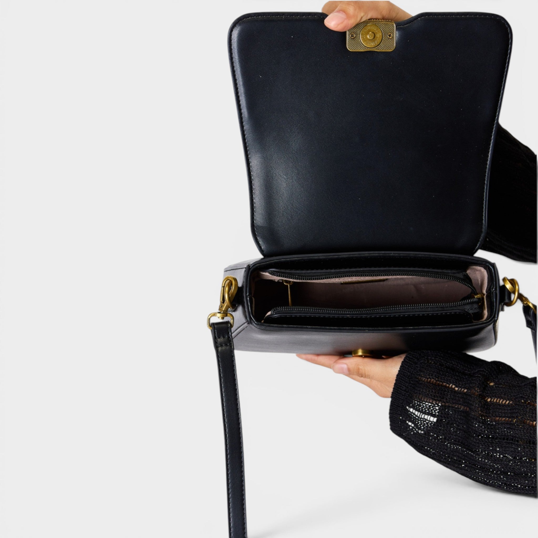 Black handbag held open by a hand on a white background