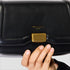 Black clutch bag with gold clasp held by a hand on a light gray background