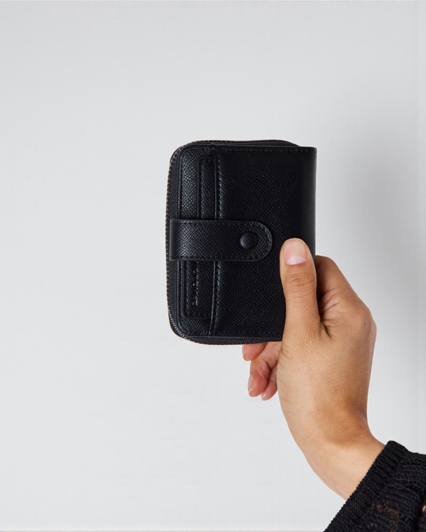 Hand holding a black wallet against a light gray background