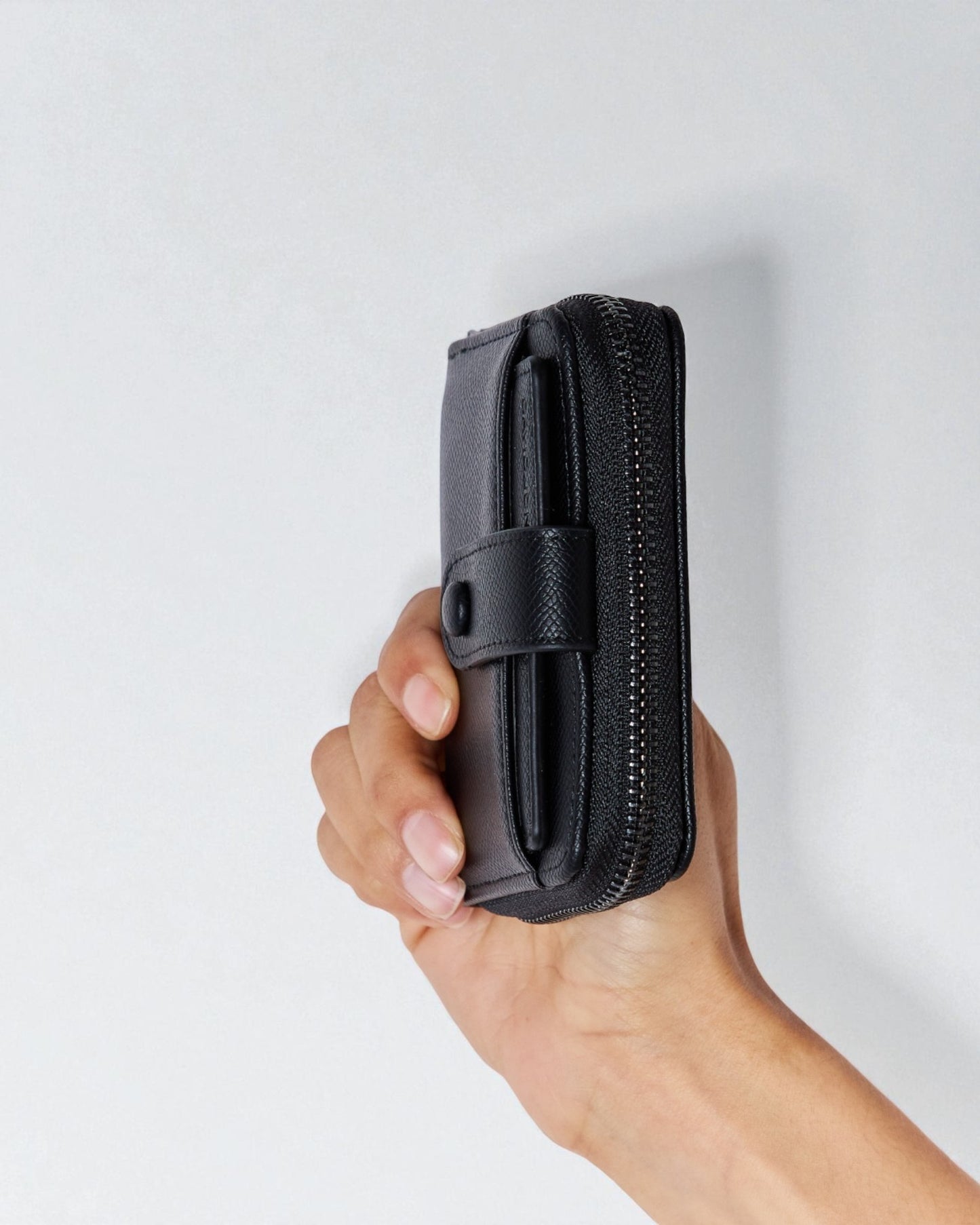 Hand holding a black wallet against a light gray background