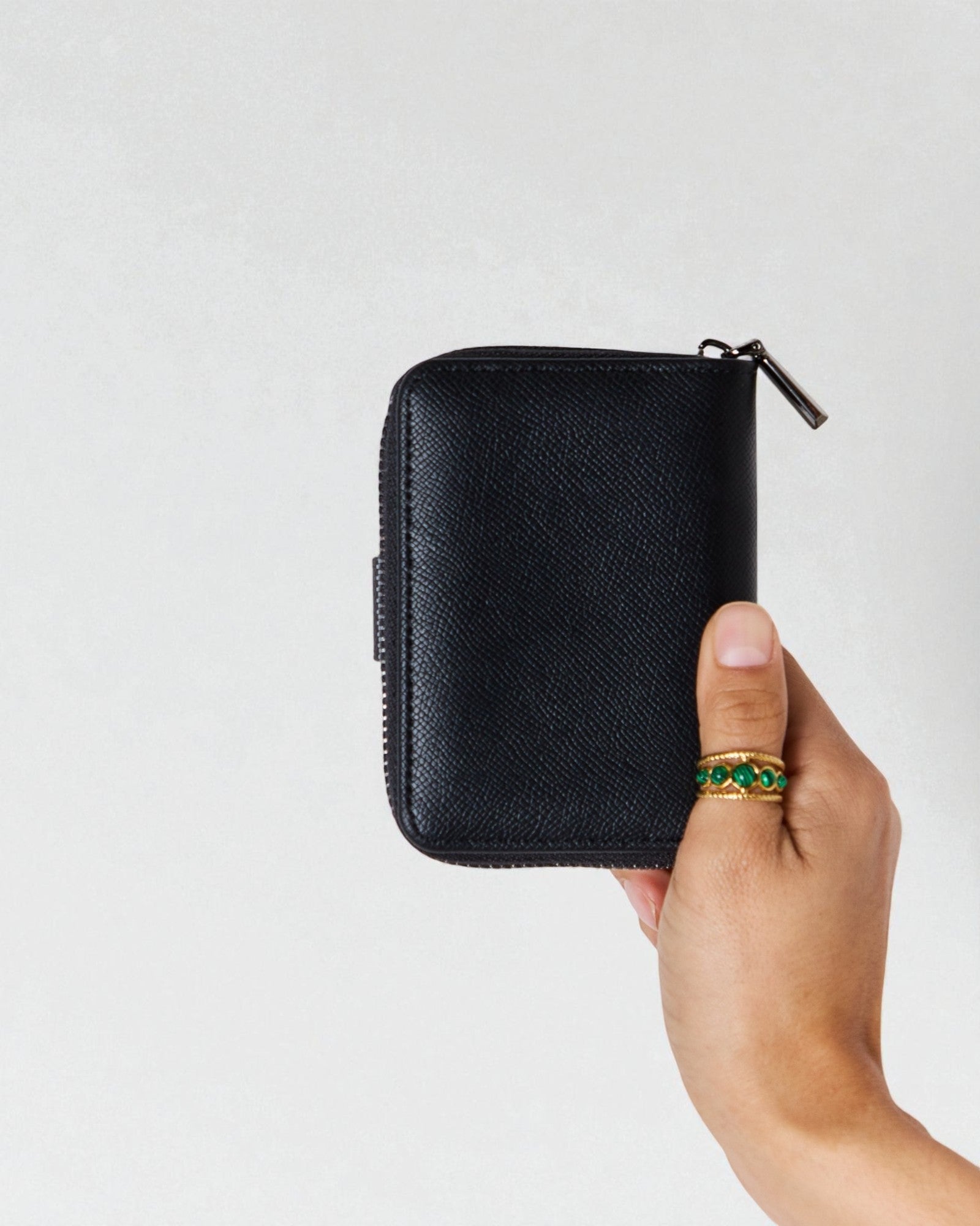 Hand holding a black zippered pouch against a light gray background