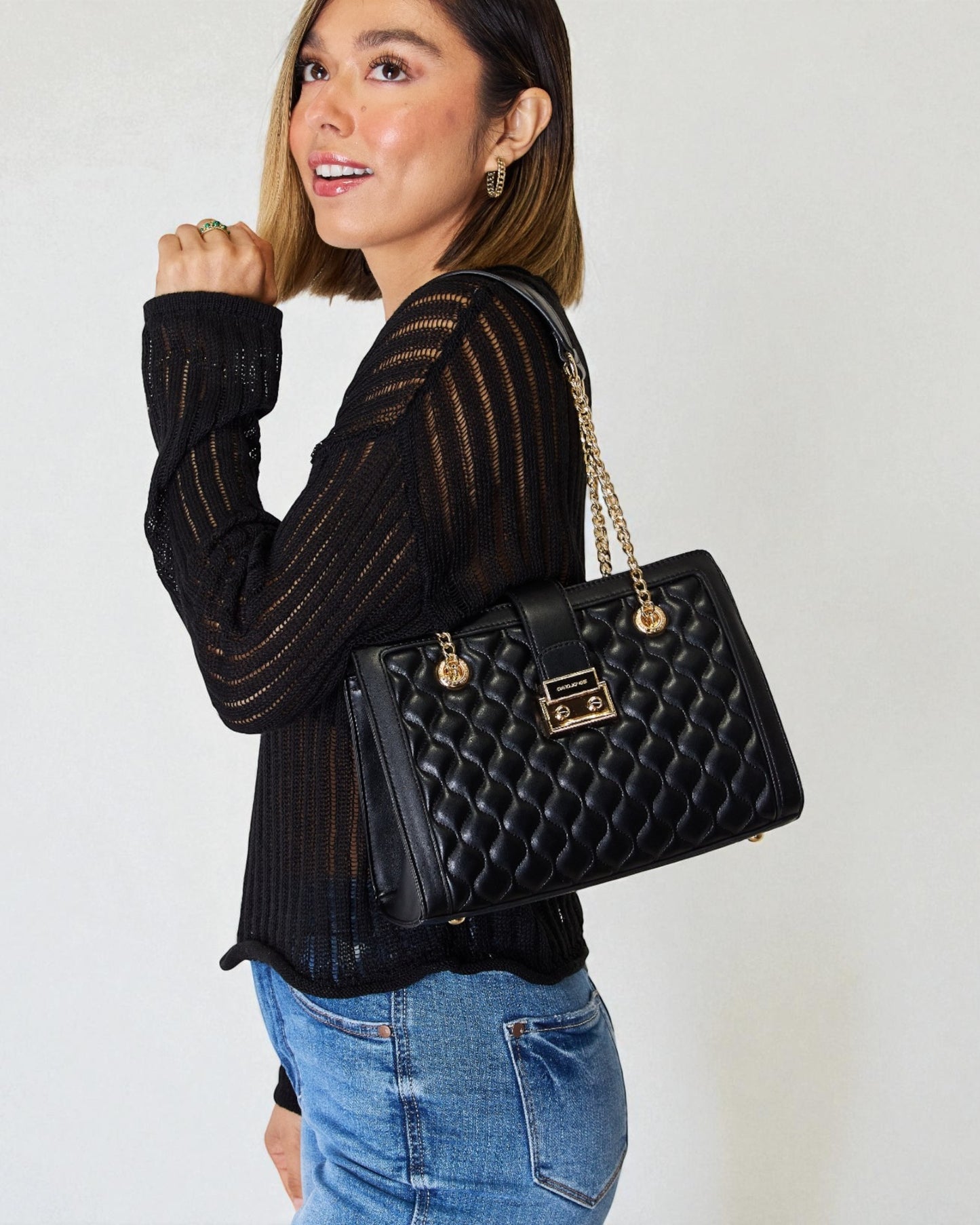 Woman holding a black quilted handbag against a plain background