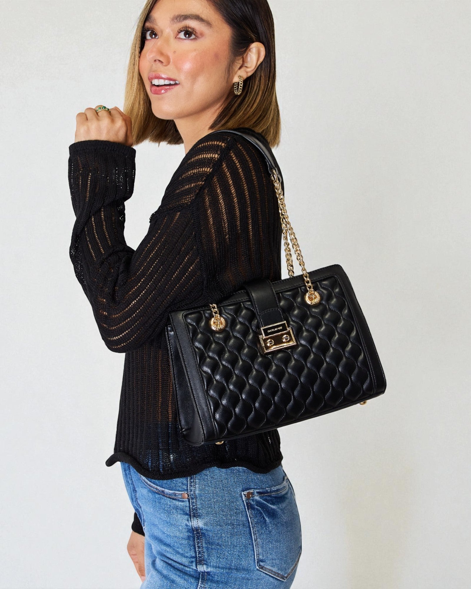 Woman holding a black quilted handbag against a plain background