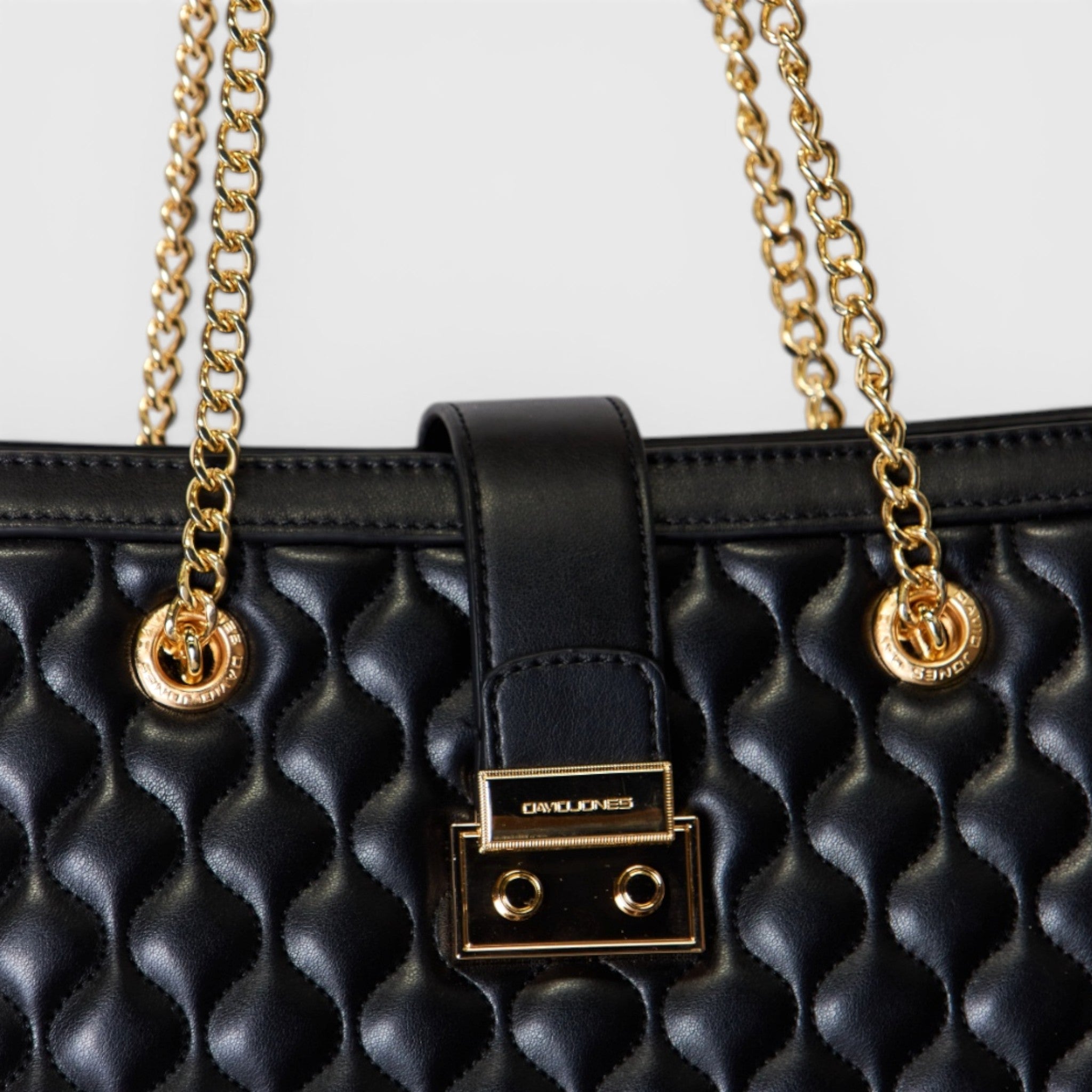 Black quilted handbag with gold chain and clasp on a light gray background