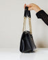 Black handbag with gold chain strap held by a hand against a neutral background