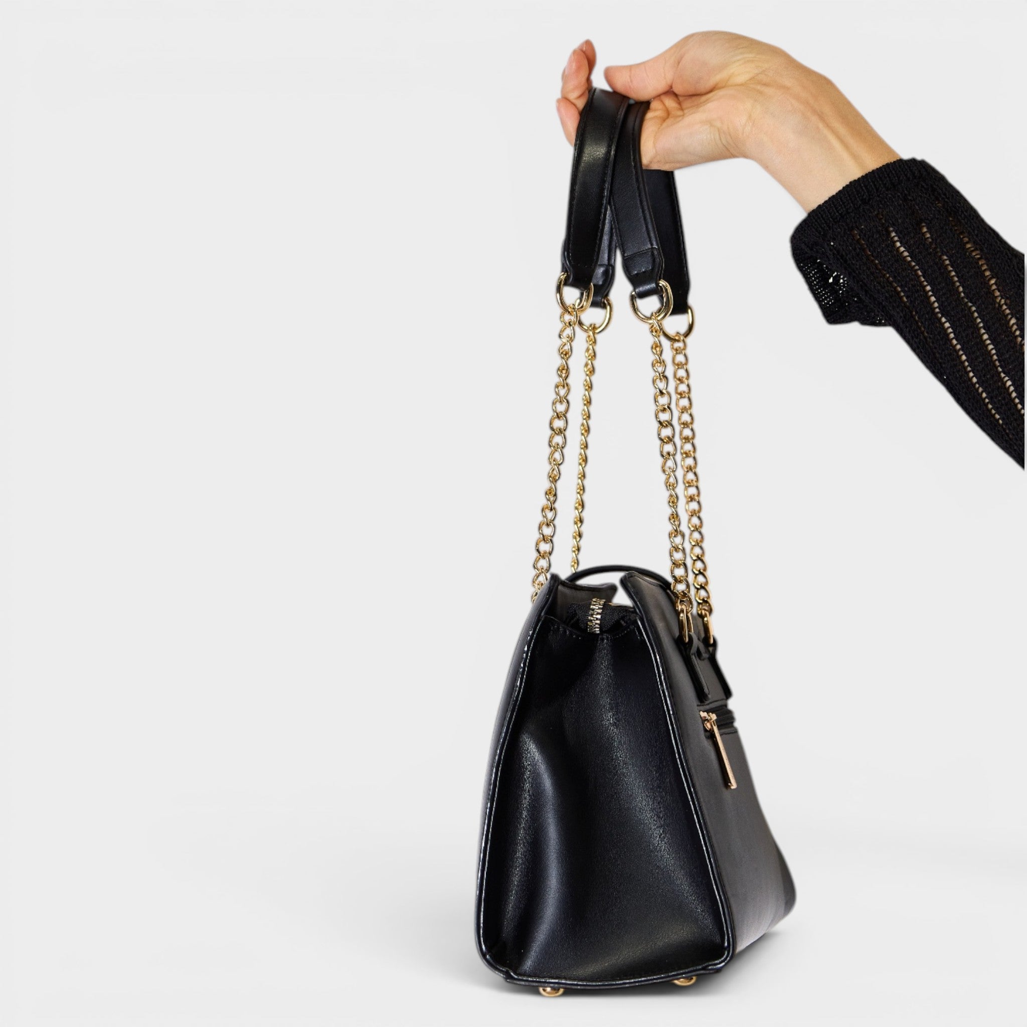 Black handbag with gold chain strap held by a hand on a light gray background