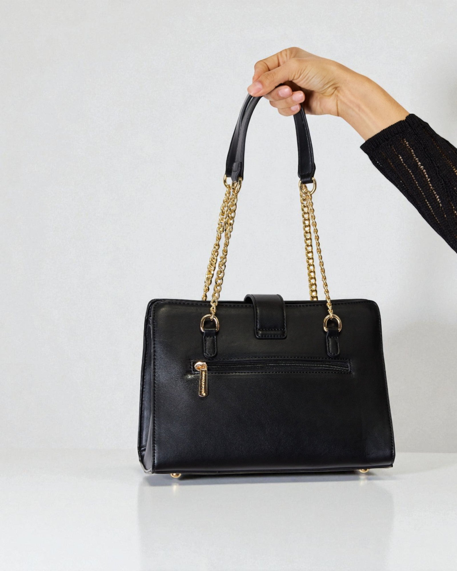 Black handbag with gold chain handle held by a hand on a white background
