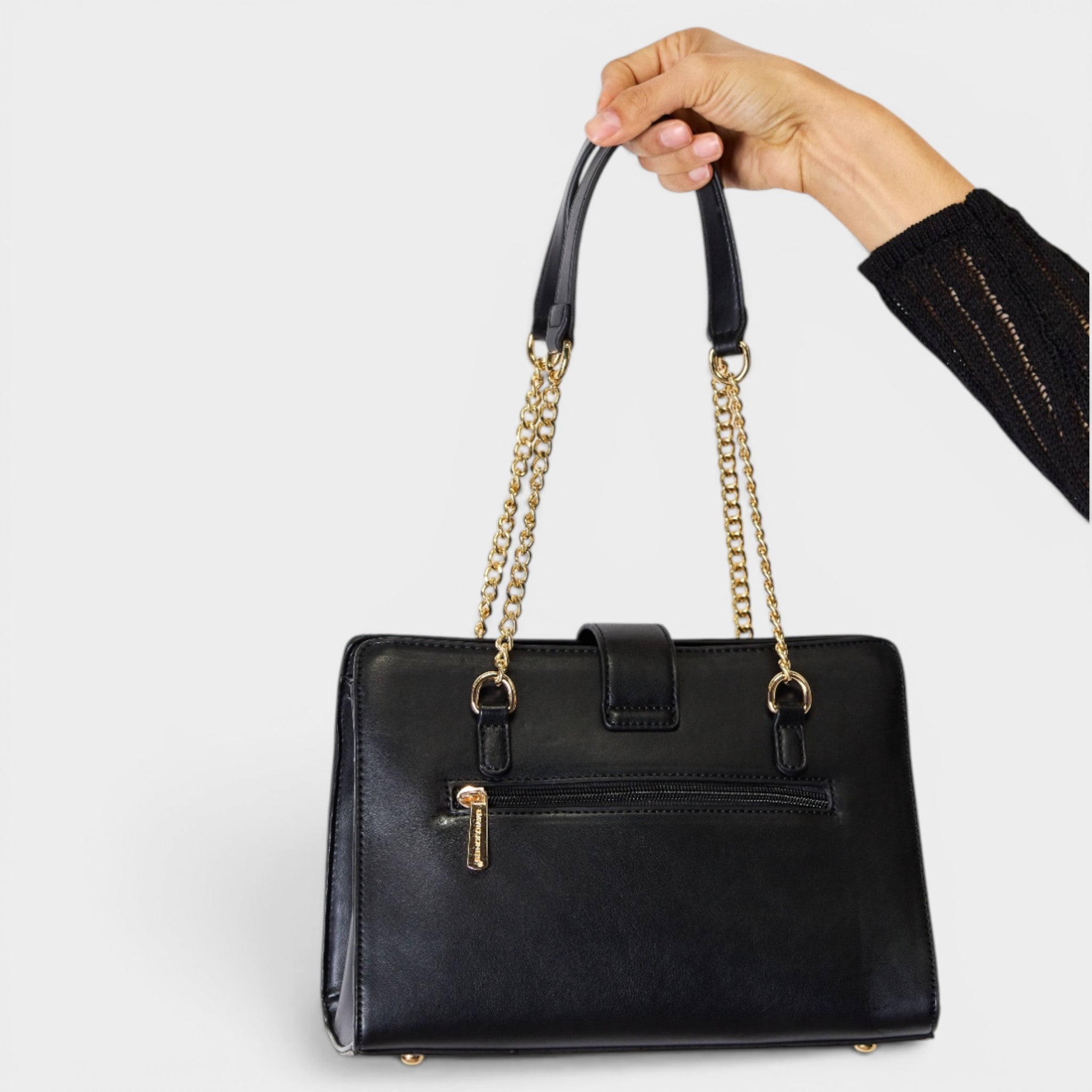 Black handbag with gold chain handle held by a hand on a light gray background