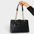 Black handbag with gold chain handle held by a hand on a light gray background