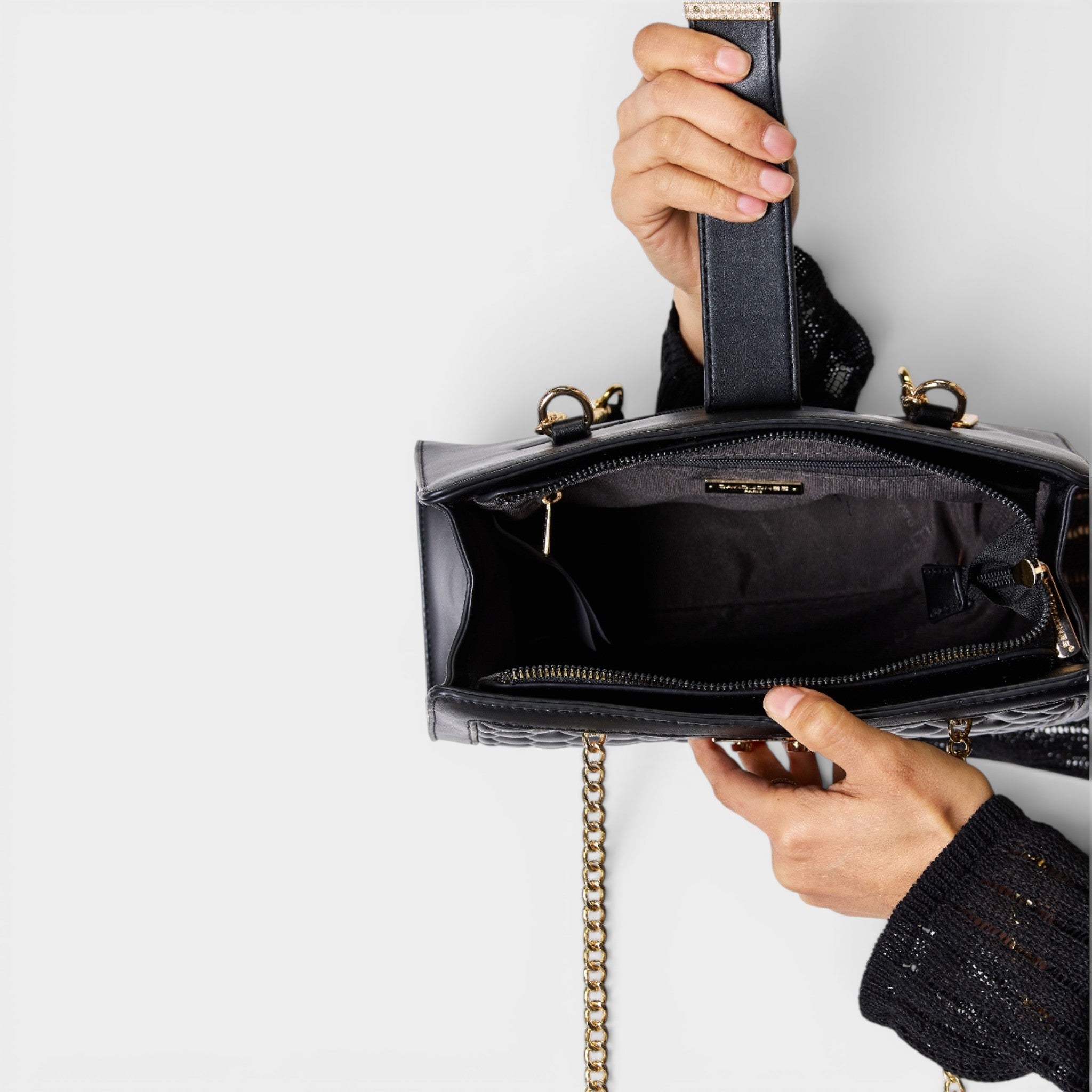 Black handbag with gold chain detail held by a person against a light gray background