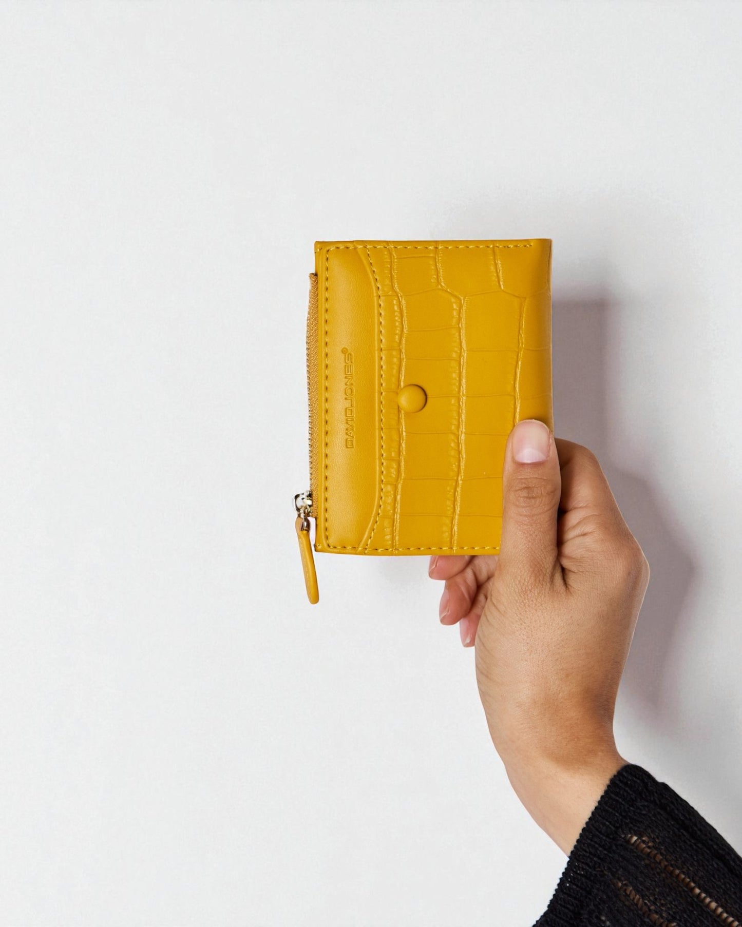 Hand holding a mustard yellow wallet against a white background