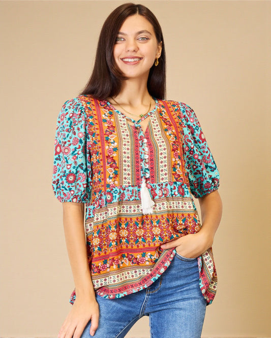 Woman wearing a colorful patterned blouse with blue jeans on a beige background