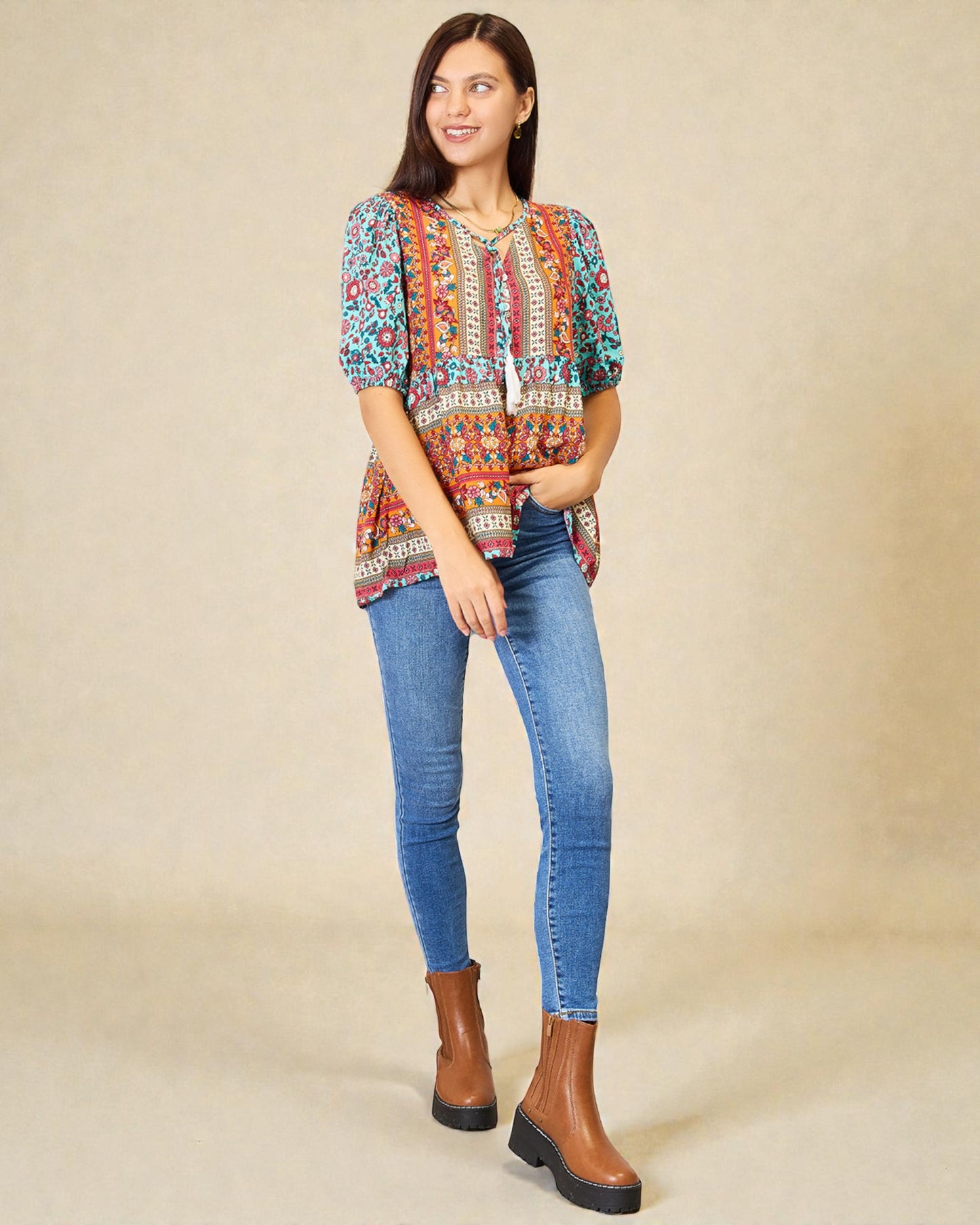 Woman wearing a colorful patterned top and blue jeans on a beige background