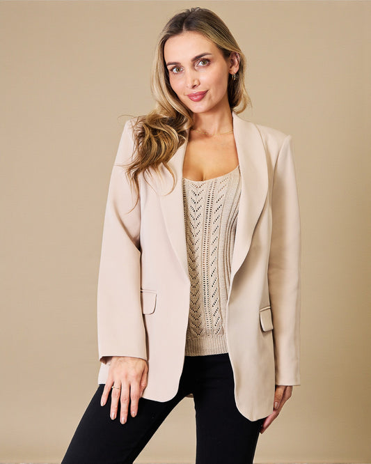 Woman wearing a beige blazer over a cable knit sweater on a beige background