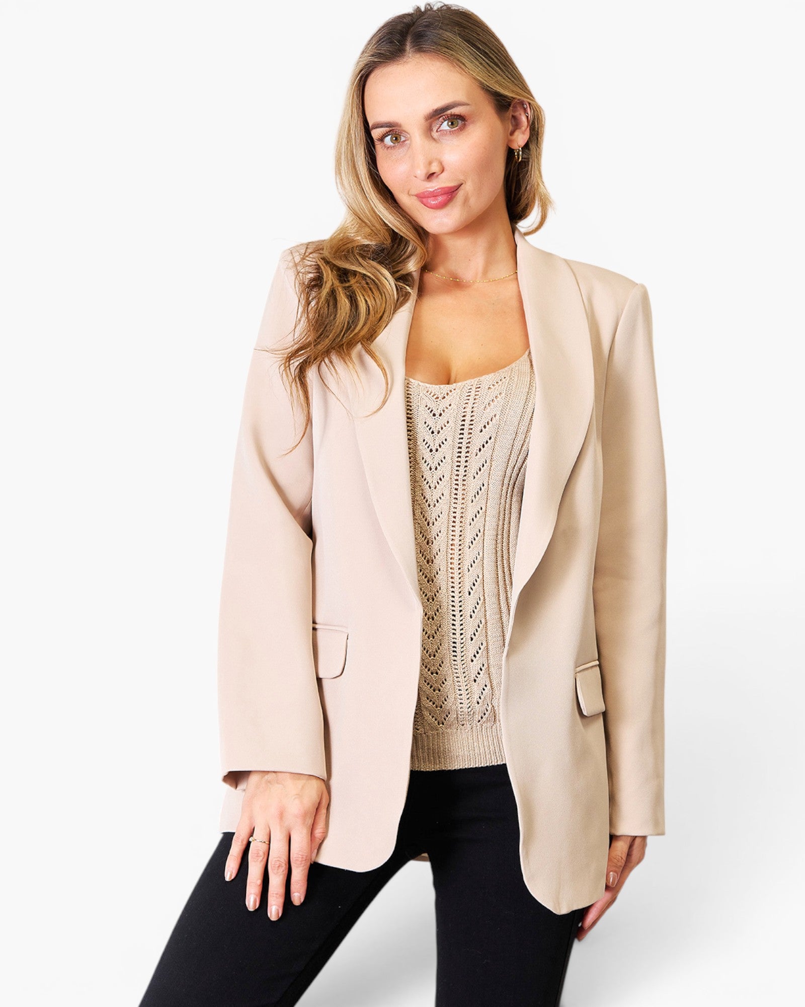 A woman modeling a light beige blazer over a beige cable-knit top and black pants, photographed against a clean white studio background.