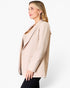 A woman shown in side profile wearing a light beige blazer over a tan top and black pants, photographed against a clean white studio background.