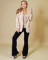 Woman wearing a beige blazer, black pants, and a white top against a beige background