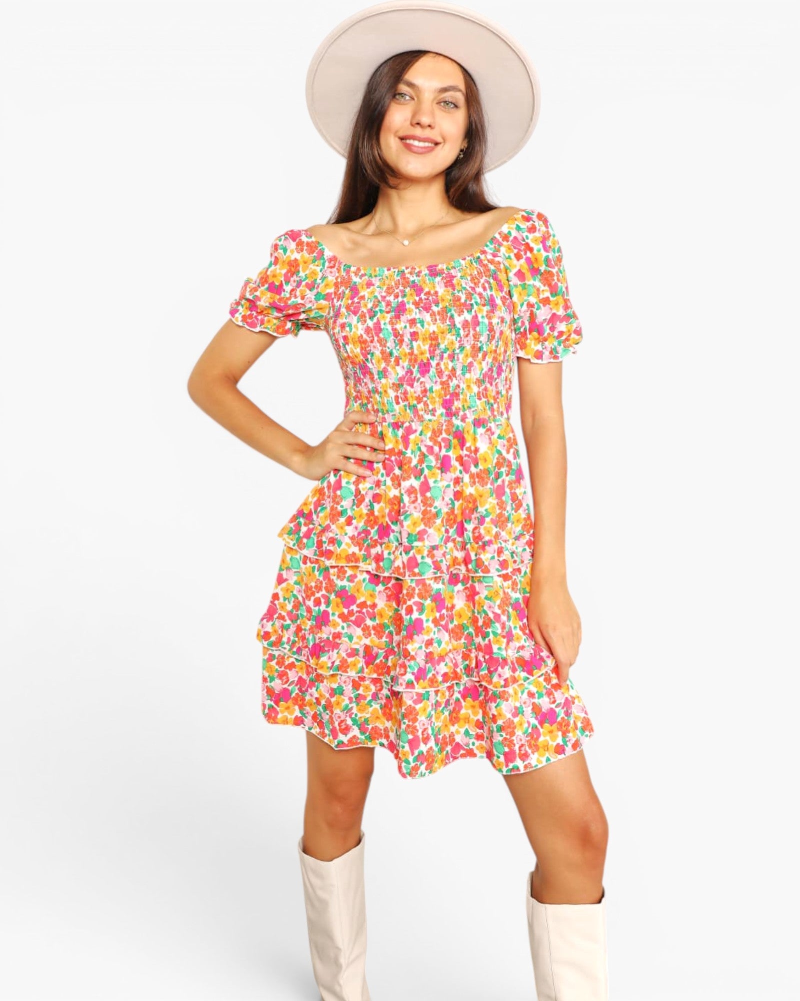 A woman modeling a short-sleeve, tiered mini dress with a vibrant multicolor floral print, styled with a wide-brimmed cream hat and cream boots against a plain white background.