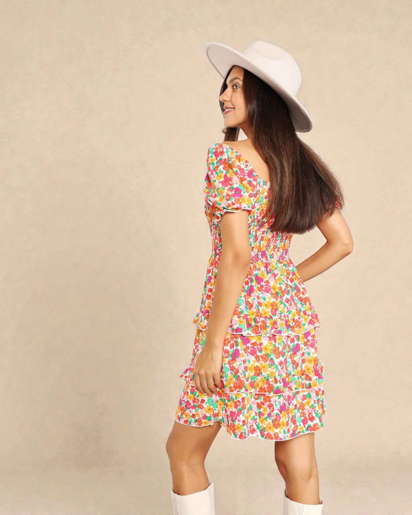 Woman wearing a colorful floral dress and white hat on a beige background