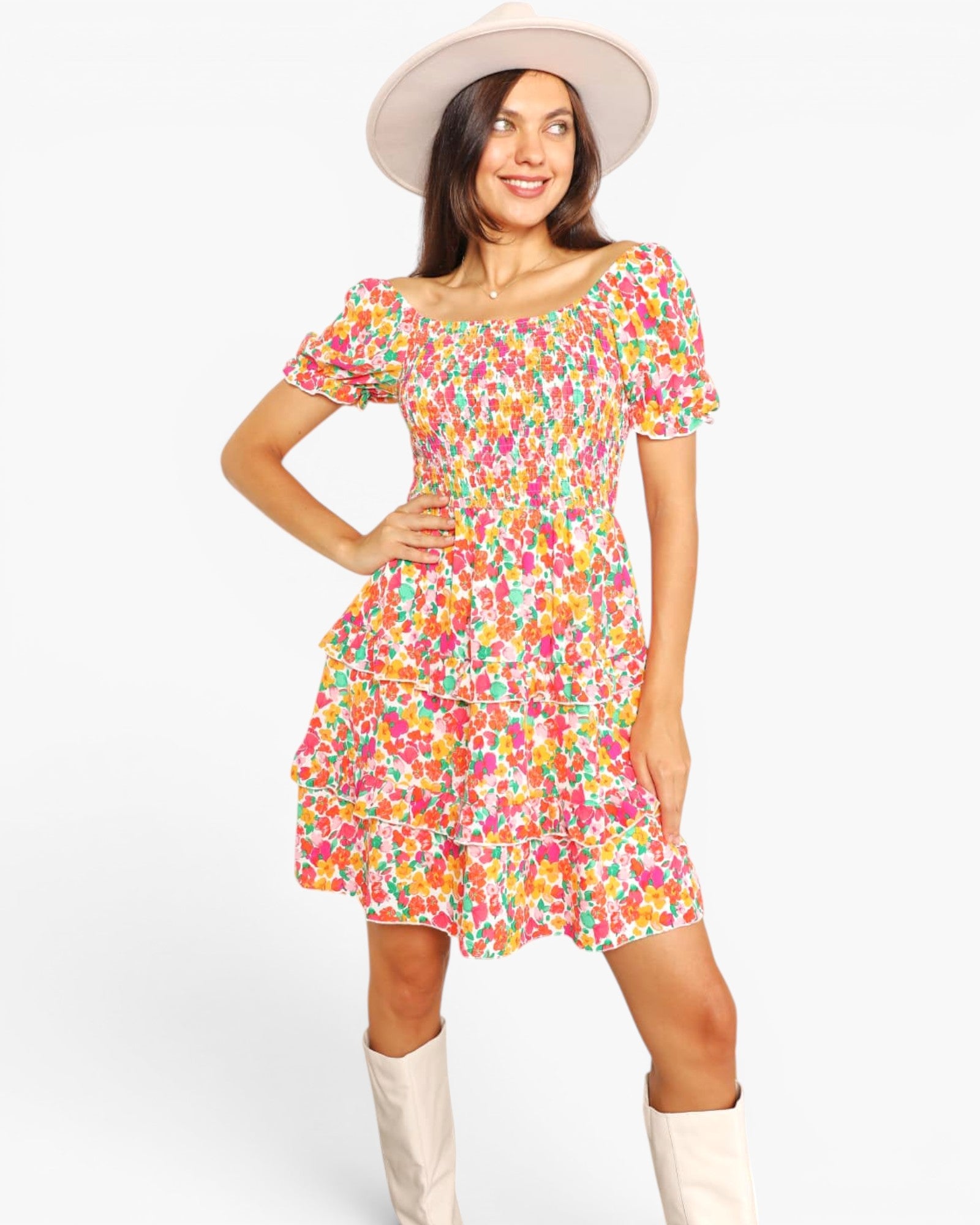 A woman modeling a short-sleeve, ruffled mini dress with a vibrant multicolor floral print on a white background, styled with a cream wide-brim hat and cream boots against a light gray studio background.