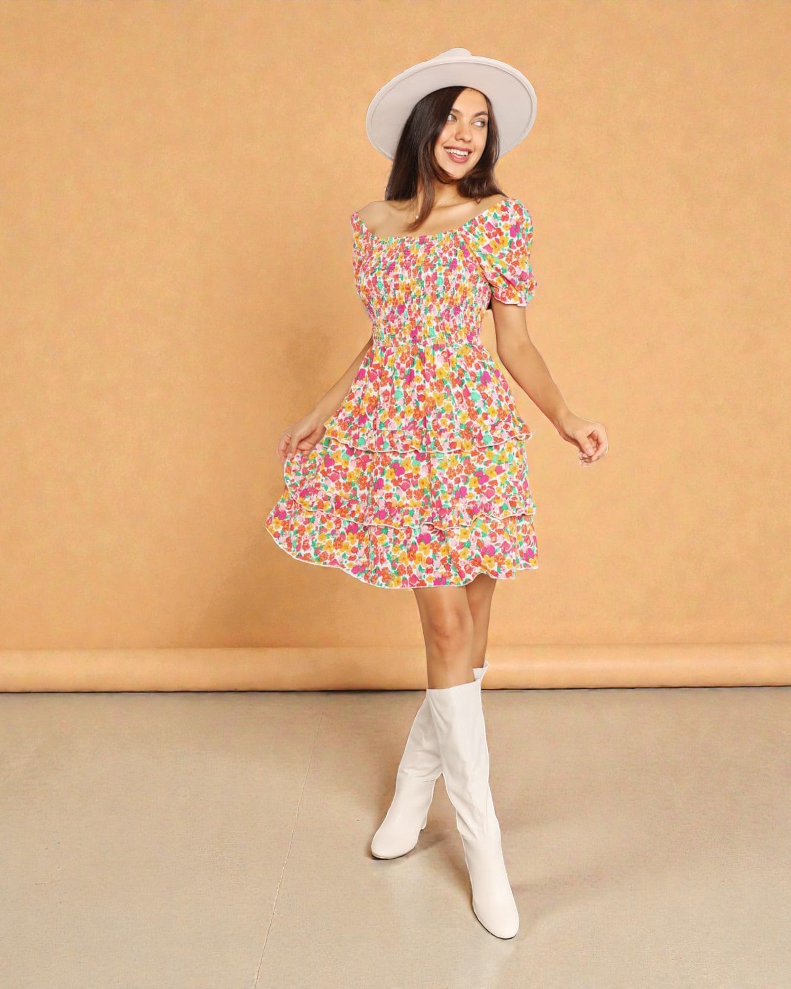 Woman wearing a colorful floral dress with white knee-high boots and a white hat against a beige background