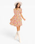 A woman modeling a short puff-sleeve dress with a colorful floral print, paired with a cream wide-brim hat and cream knee-high boots, against a plain white studio background.