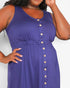 A close-up of a woman wearing a sleeveless purple dress with a button-down front and a gathered elastic waist, set against a plain light background.