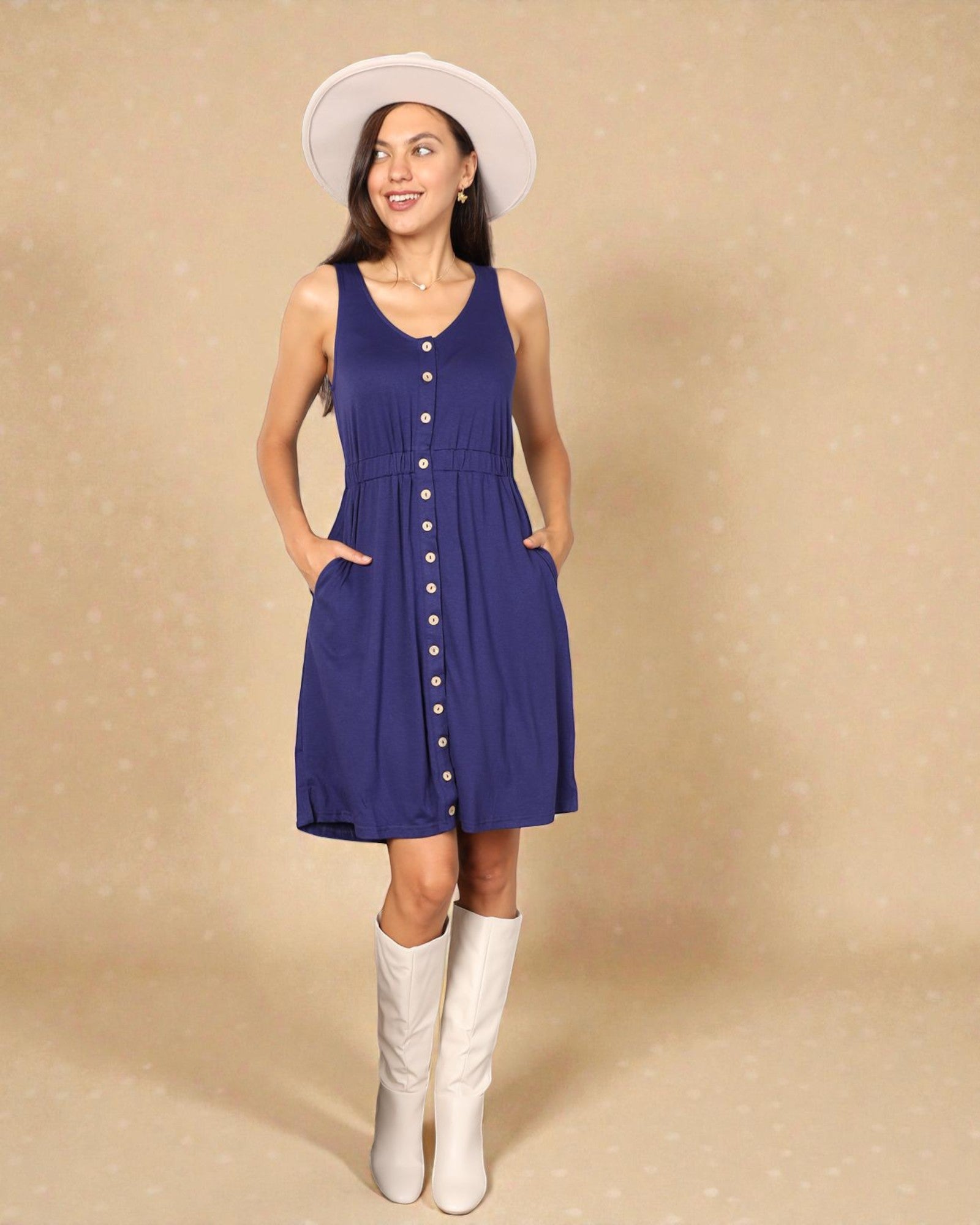 Woman wearing a blue dress with buttons, white boots, and a white hat on a beige background