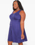 A woman modeling a sleeveless purple babydoll dress with a button-down front and an elastic waistband, set against a plain white studio background.