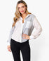 A woman modeling a color-blocked long-sleeve button-up shirt with a light gray heathered body, white front placket and pocket, and a pale blush-beige sleeve, paired with black pants against a plain white background.