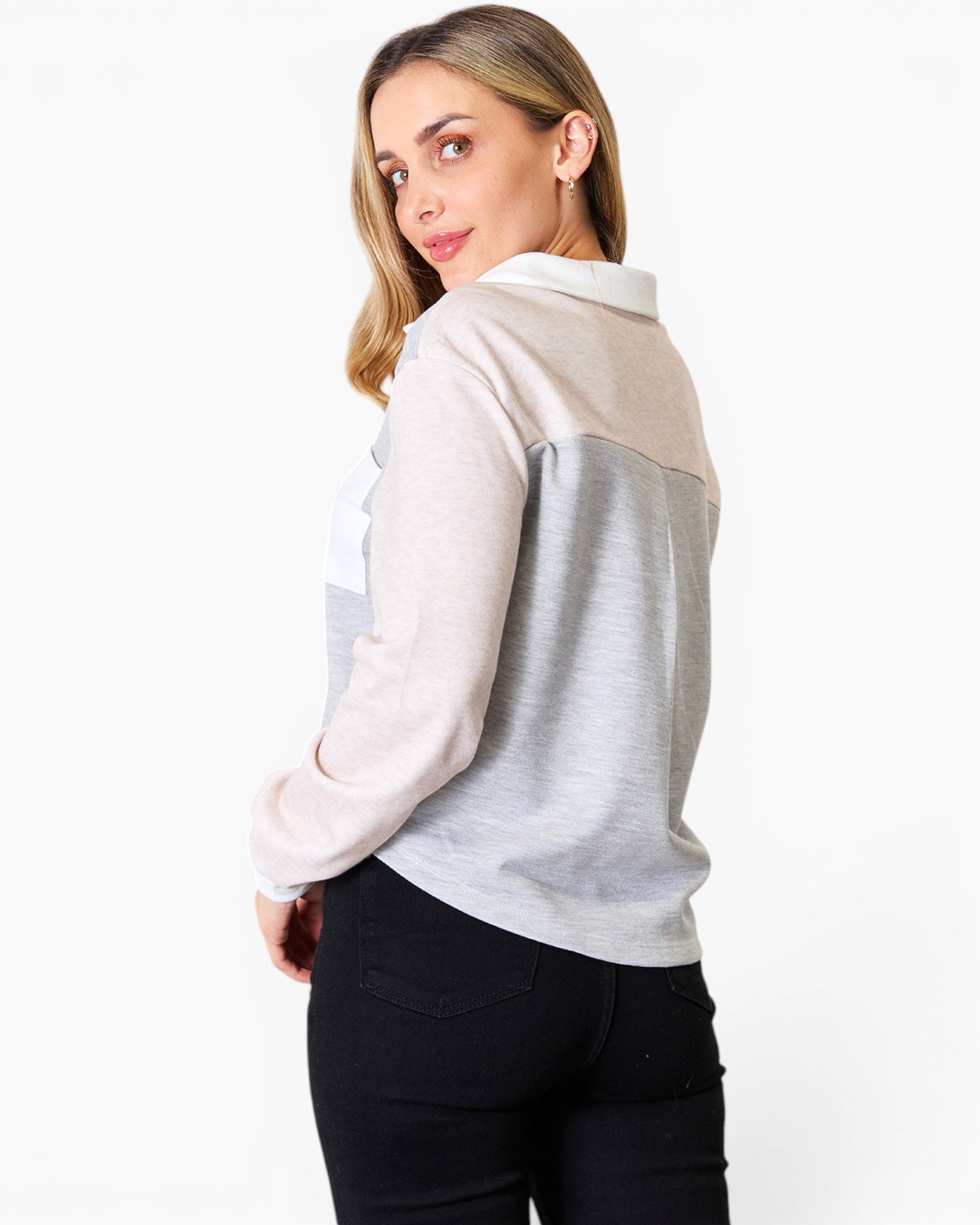 A woman wearing a color-blocked long-sleeve top with a white collar, featuring light beige, light gray, and white panels, paired with black pants, photographed against a plain white background.