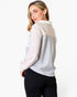 A woman wearing a color-blocked long-sleeve top with a white collar, featuring light beige, light gray, and white panels, paired with black pants, photographed against a plain white background.