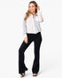 A woman modeling a light gray and white color-blocked button-up shirt with black flared pants and black sandals, photographed against a clean white studio background.