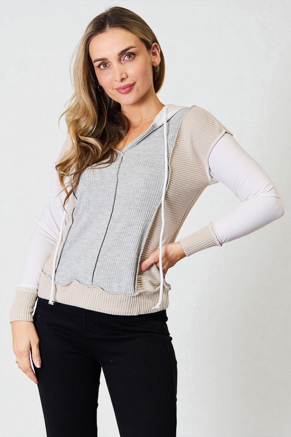 Woman wearing a light gray zip-up hoodie with beige sleeves on a white background