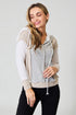 Woman wearing a light-colored hoodie with a mesh design on a plain background