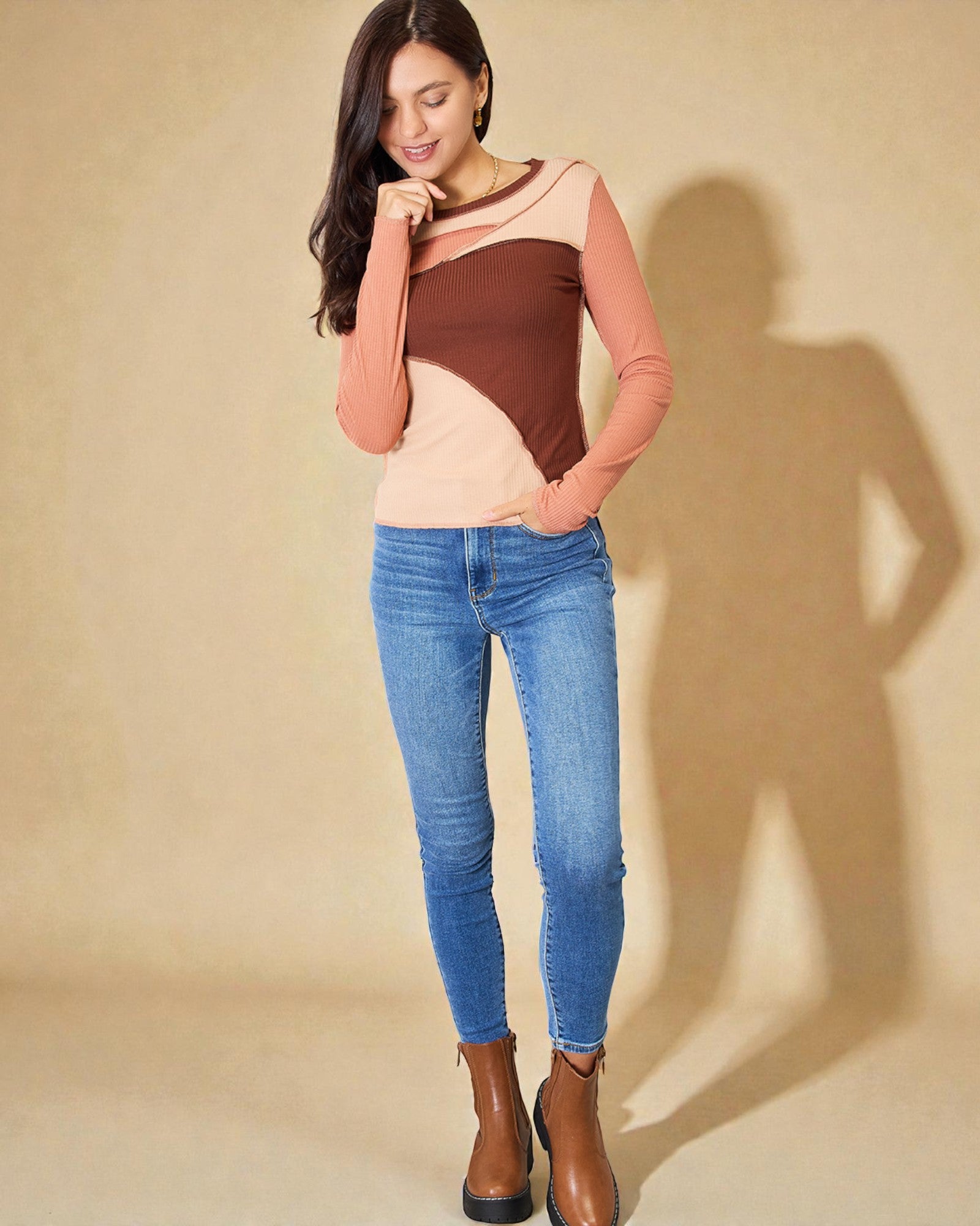 Woman wearing a color-blocked top and blue jeans against a beige background