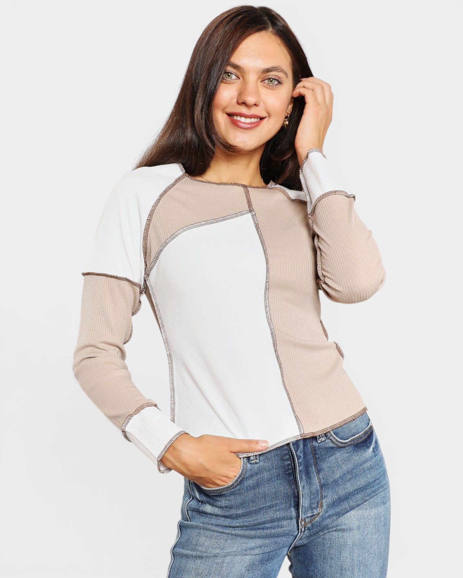 Woman wearing a beige and white long-sleeve top with blue jeans on a light gray background
