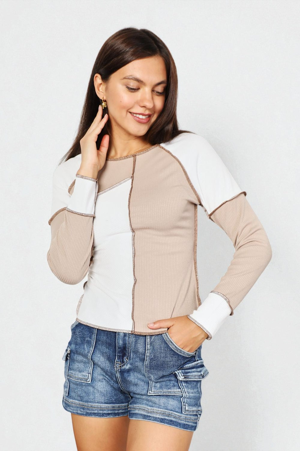 Woman wearing a two-tone jacket with beige and white sleeves, paired with denim shorts on a plain background.