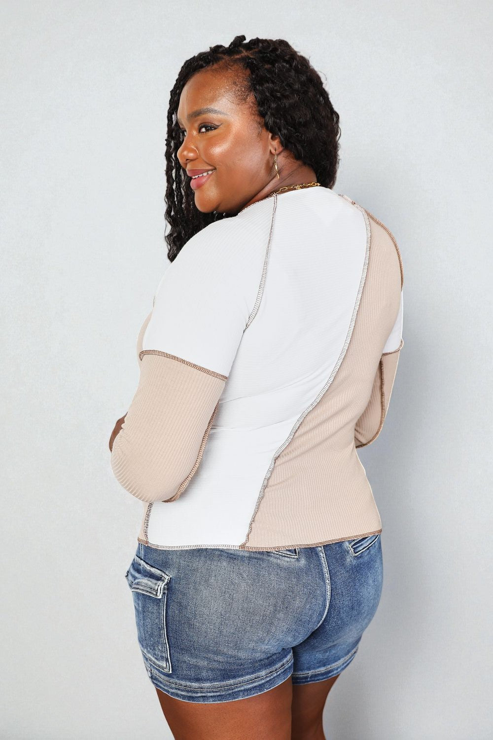 Woman wearing a two-tone shirt and denim shorts against a white background