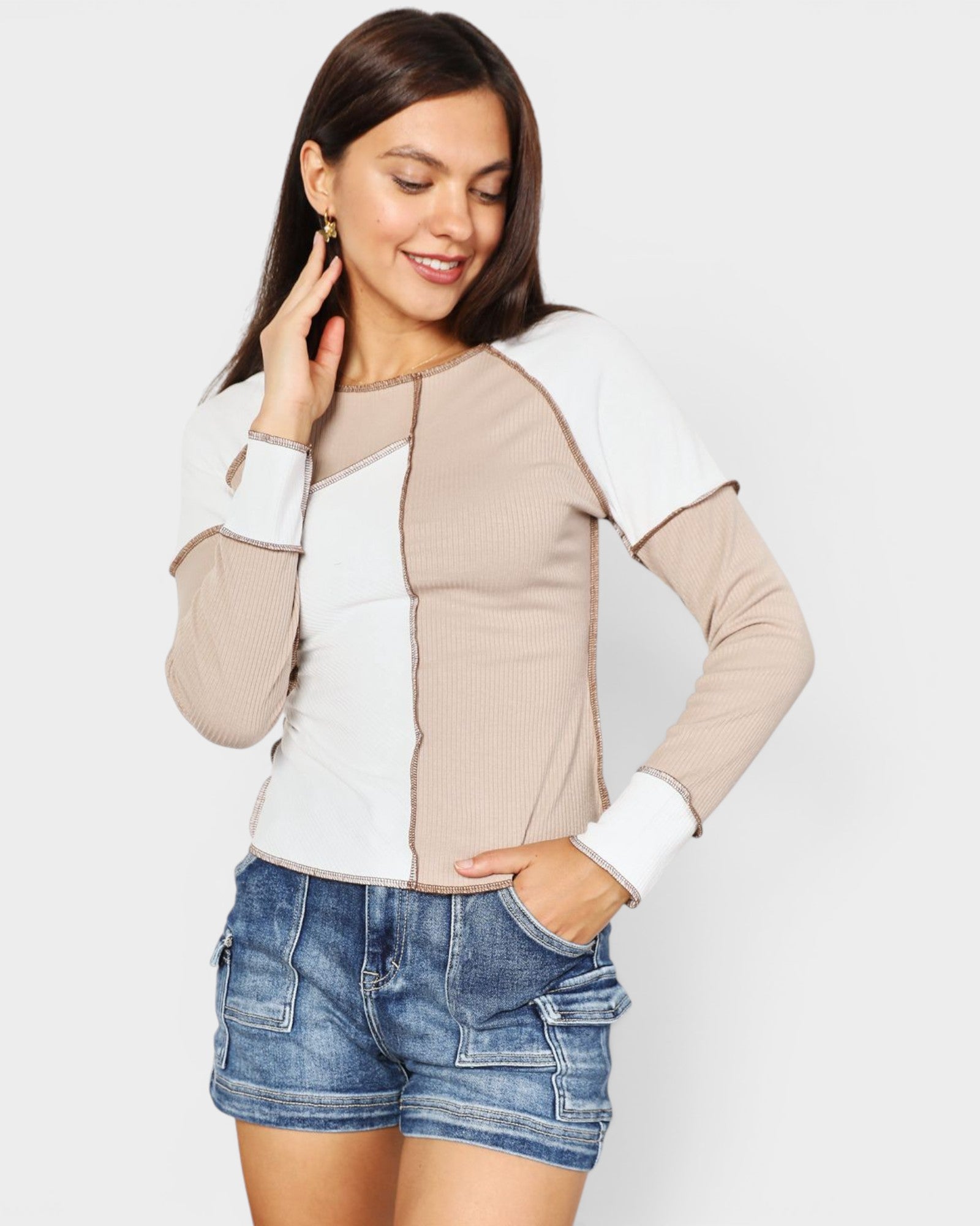 Woman wearing a beige and white long-sleeve top with denim shorts on a light gray background
