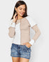 Woman wearing a beige and white long-sleeve top with denim shorts on a light gray background
