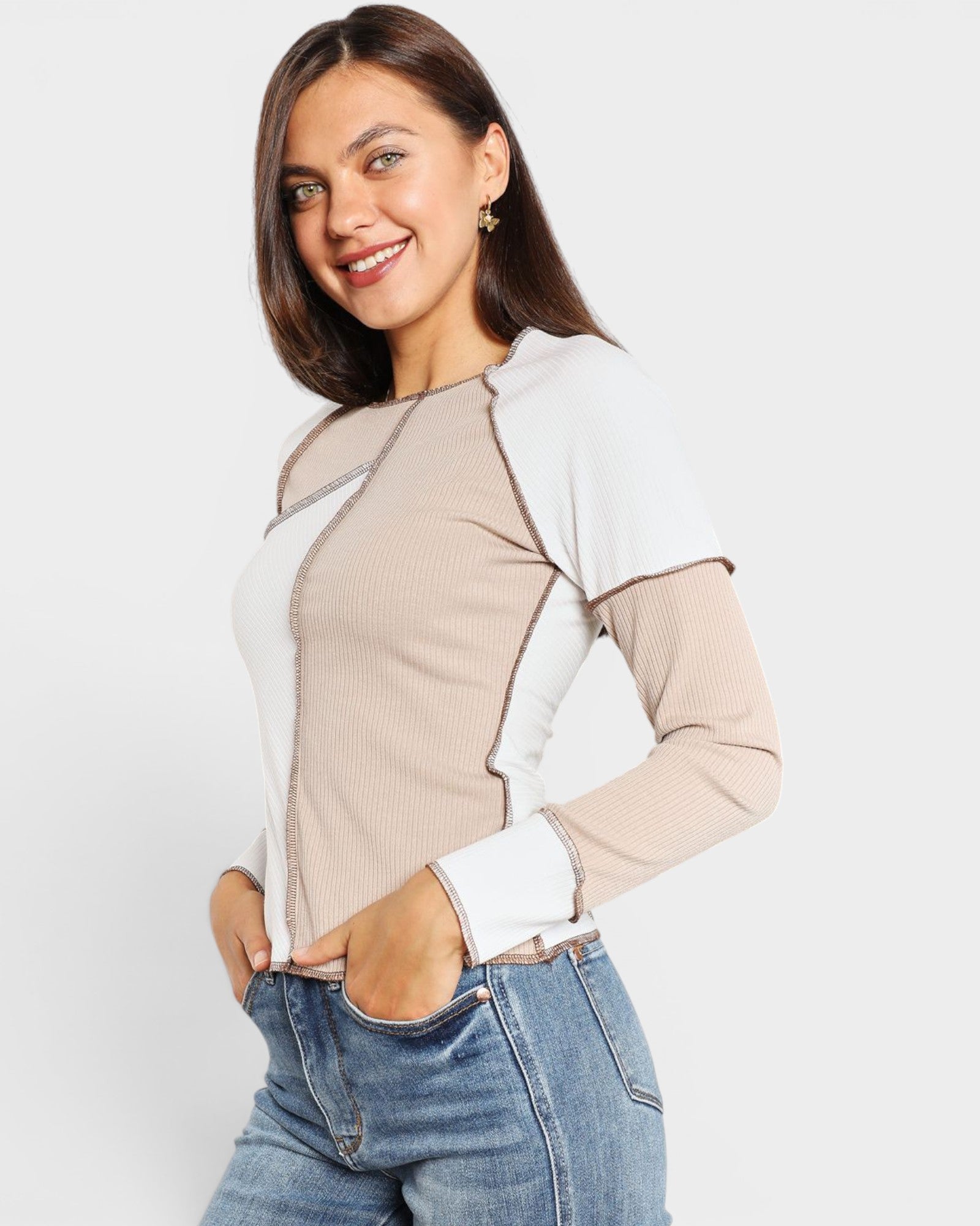 Woman wearing a two-tone shirt with beige and white sleeves and body, paired with blue jeans on a light gray background.