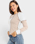 Woman wearing a two-tone shirt with beige and white sleeves and body, paired with blue jeans on a light gray background.