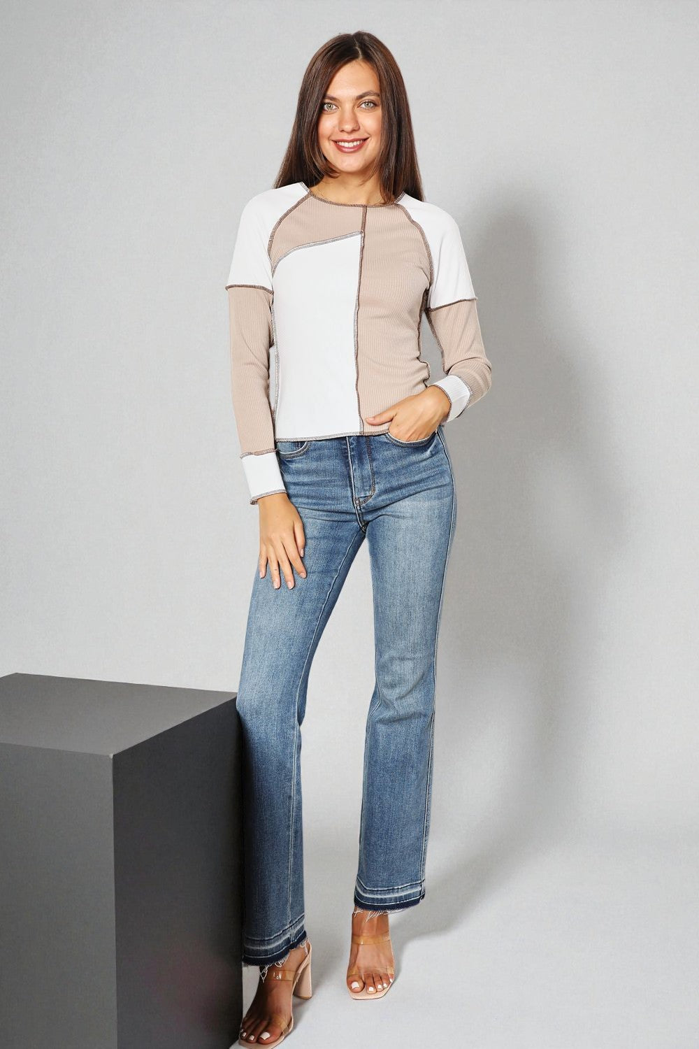 Woman wearing a color-blocked jacket and blue jeans on a gray background