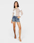 Woman wearing a beige and white top with denim shorts on a plain background