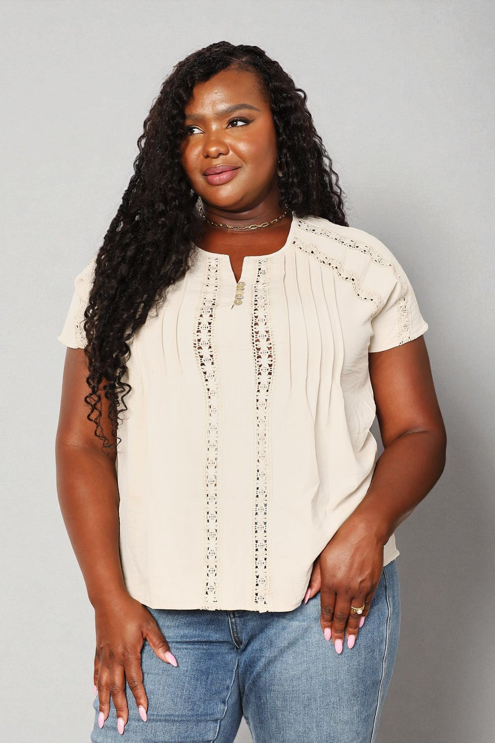 Woman wearing a beige blouse and blue jeans against a gray background