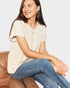 Woman wearing a beige blouse and blue jeans sitting on a brown chair against a white background