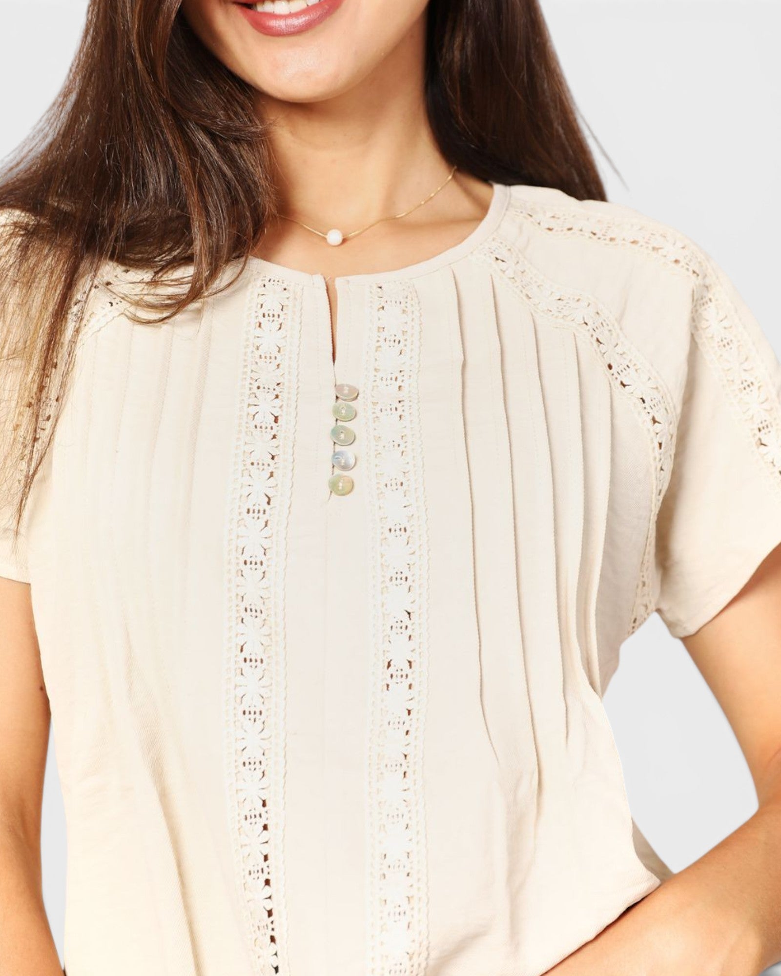Close-up of a beige blouse with lace details on a plain background