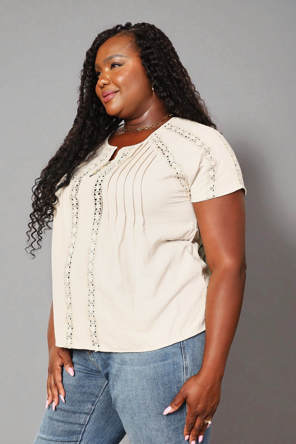 Woman wearing a beige blouse with short sleeves and blue jeans on a gray background